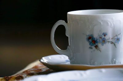 Xicara de café branca com flores azuis desenhadas sobre um pano marrom